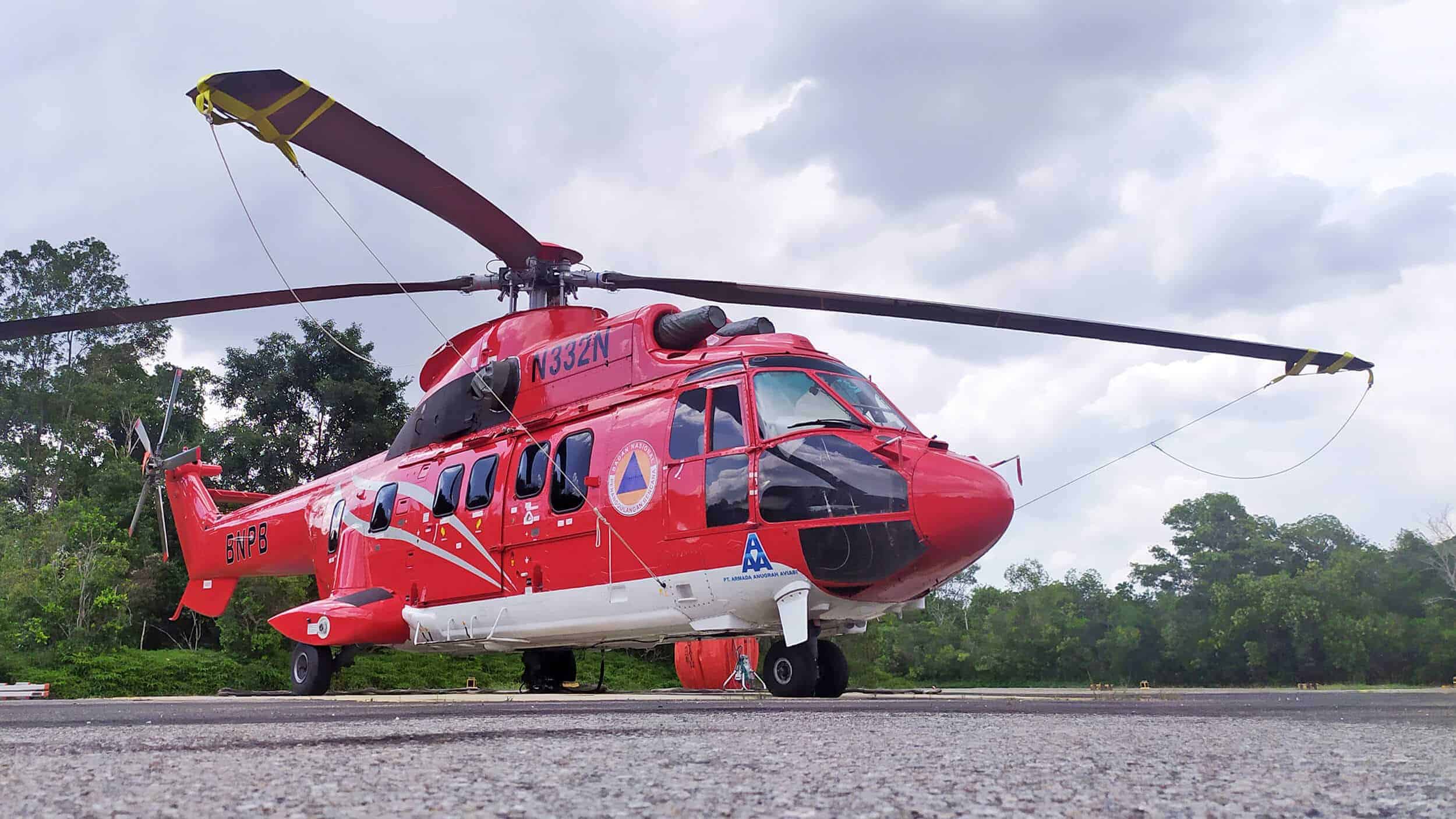 A large red helicopter from Nomad Aviation is parked on a concrete helipad with trees and cloudy skies in the background, showcasing the versatility of helicopters for construction in South East Asia.