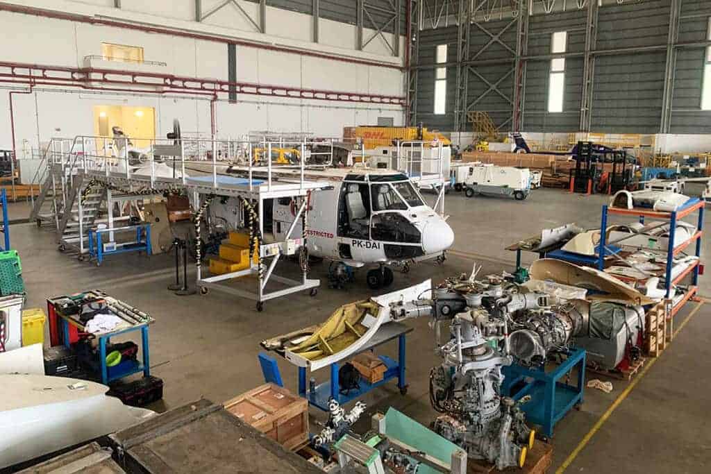 Aircraft maintenance hangar with a small plane being serviced and various equipment and parts around.