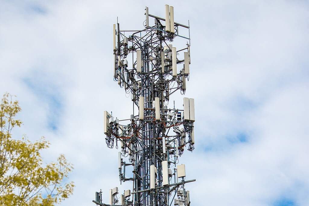 Cellular tower with multiple antennas against a partly cloudy sky, some tree branches visible—vital for nomad aviation and south east asia disaster relief communication efforts.