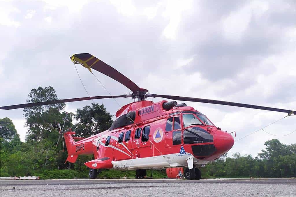 A red rescue helicopter is parked on a runway with trees and clouds in the background.